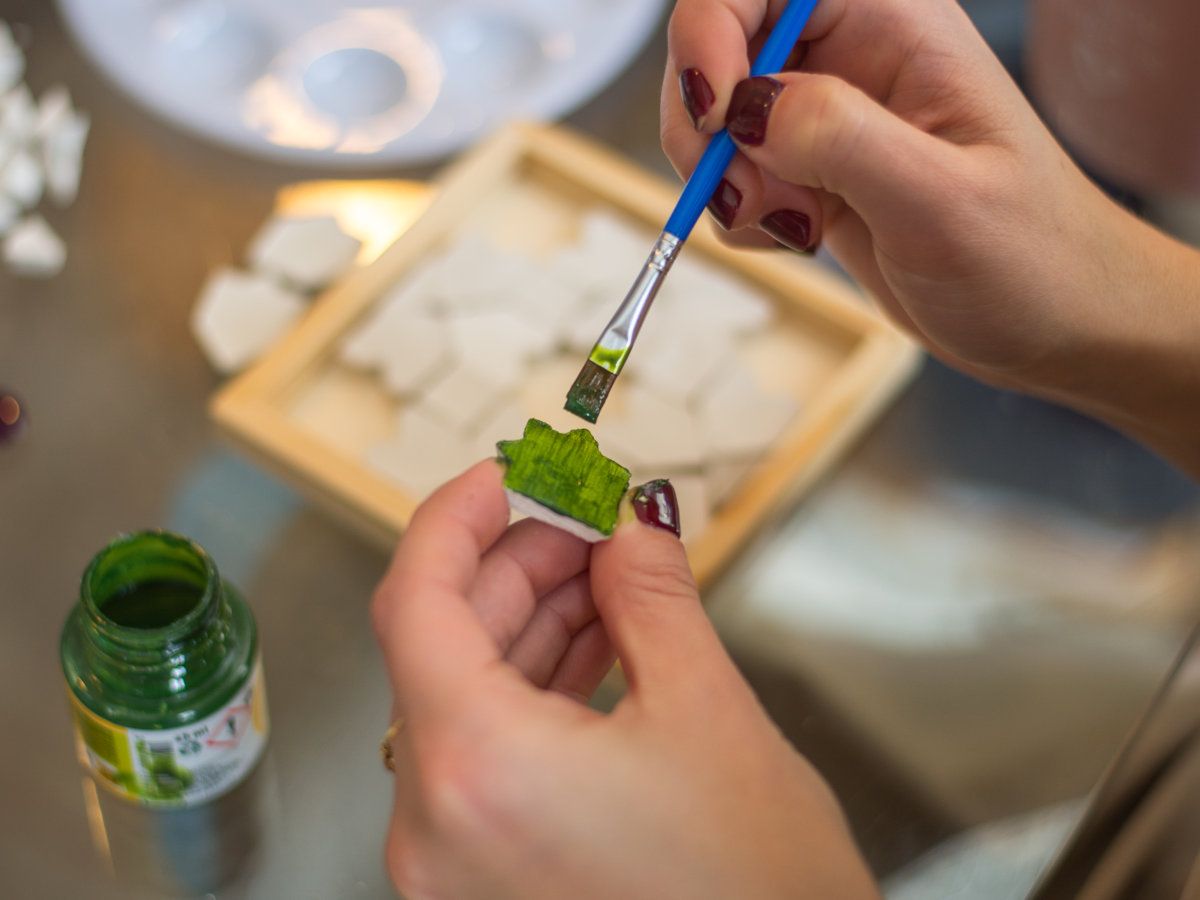 Painting a clay tile green with a fine brush